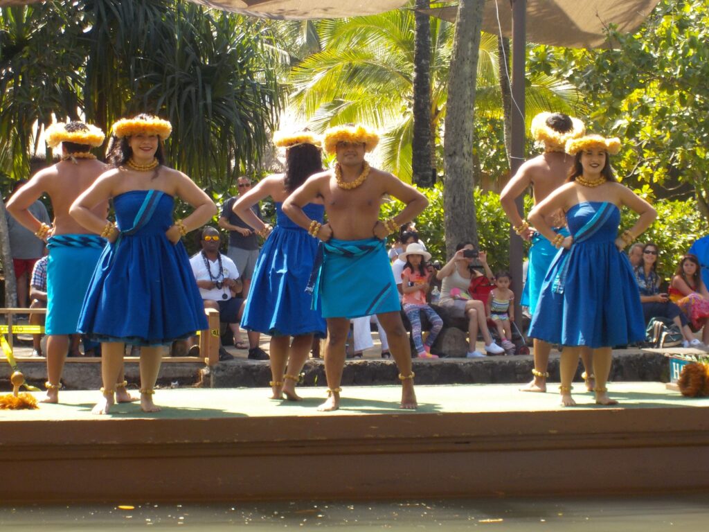 Dancers in blue skirts and yellow headpieces perform on an outdoor stage.