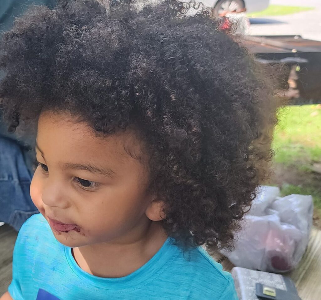 Young child with curly hair wearing a blue shirt outdoors.