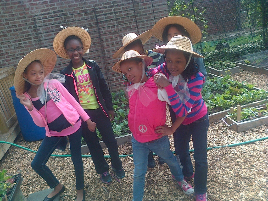 Five children wearing hats and colorful clothes posing outdoors.