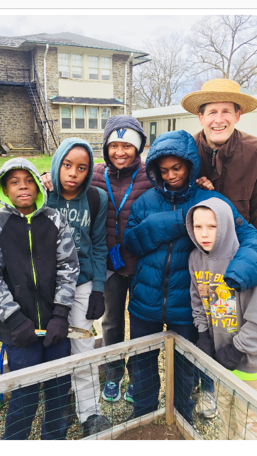 A group of boys and a man smiling outdoors by a fence.